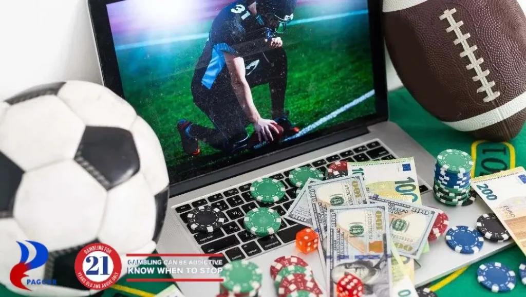 A laptop showing an American football game surrounded by a betting chips, dice, cash, and sports equipment on a table.